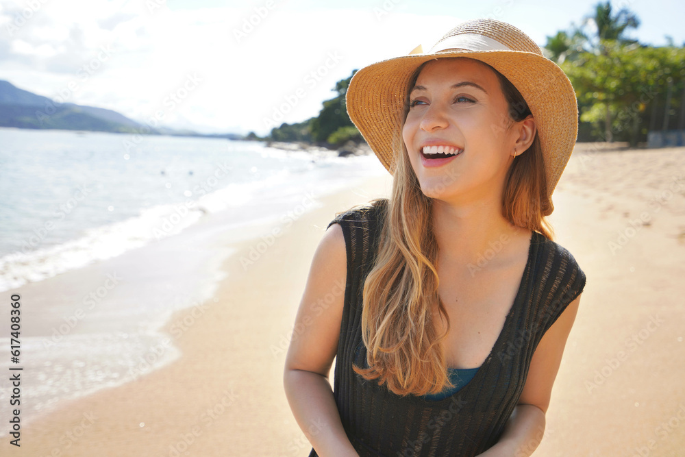 Close-up of a beautiful young woman wearing summer dress and straw hat on the tropical beach
