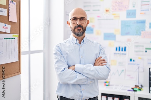 Young bald man business worker standing with arms crossed gesture at office