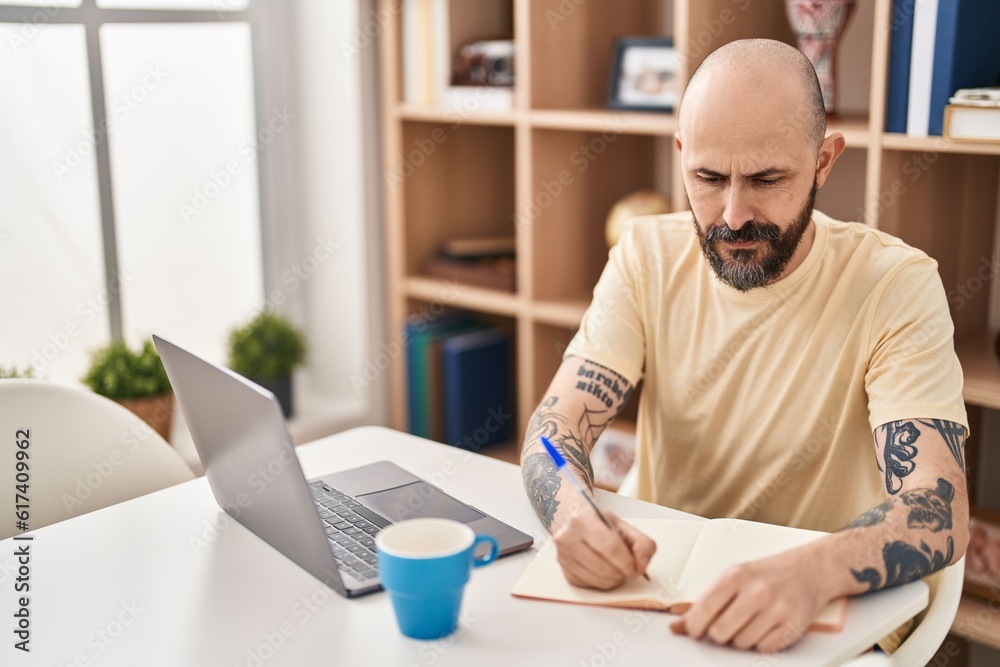 Young bald man sitting on table studying at home Young bald man sitting on table studying at home