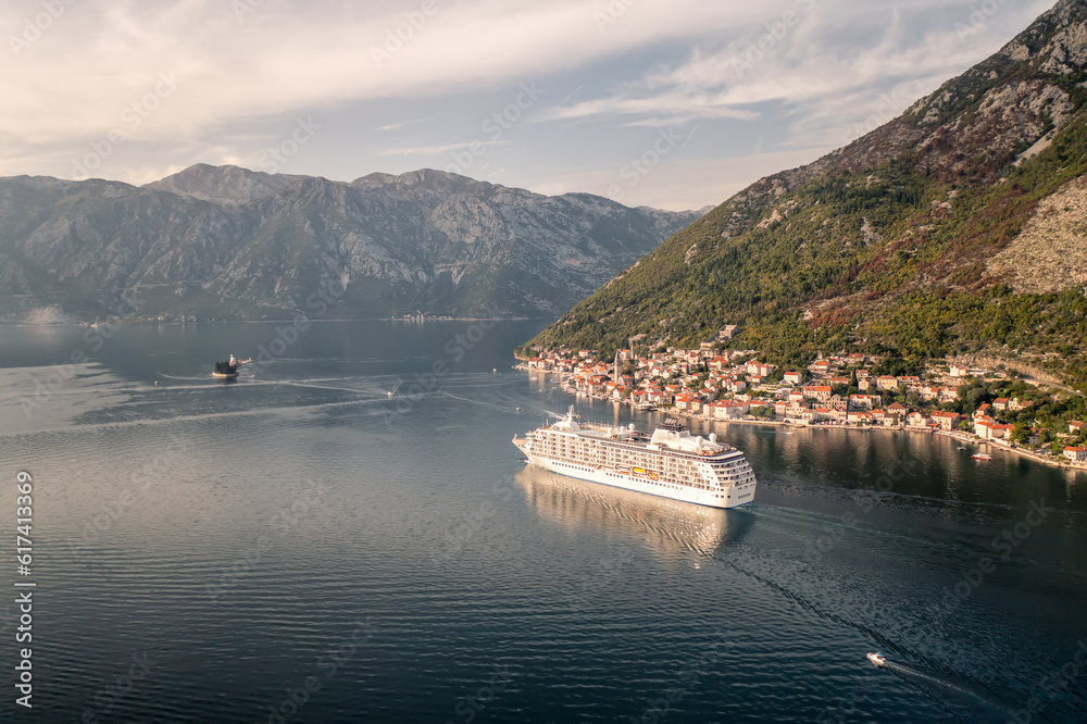 Aerial panoramic view of the picturesque town of Perast with islands and a large cruise ship passing near it in the waters of the Bay of Kotor in sunny day, Montenegro.