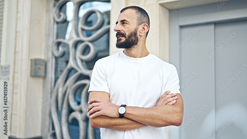 Young hispanic man standing with crossed arms looking to the side at street Young hispanic man standing with crossed arms looking to the side at street