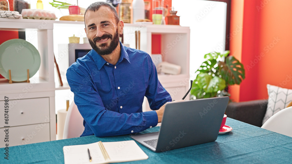 Young hispanic man using laptop smiling at dinning room
