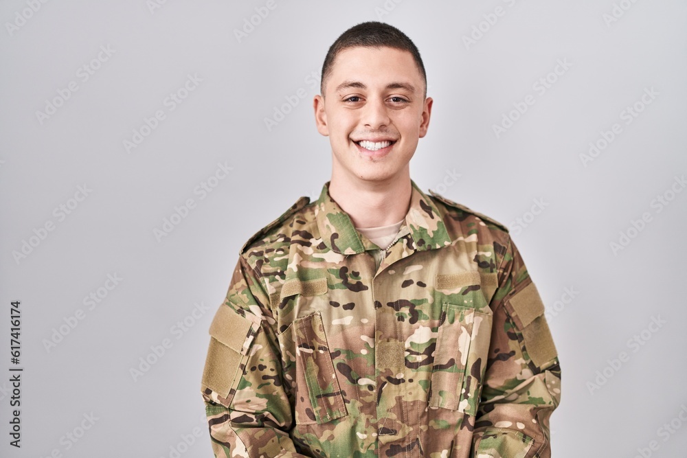 Young man wearing camouflage army uniform with a happy and cool smile on face. lucky person.