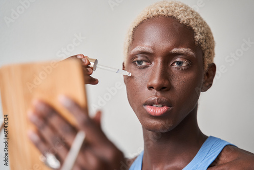 Close up portrait of blonde handsome guy holding glass dropper and mirror