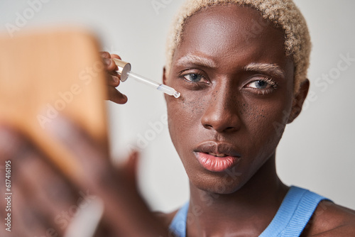 Close up of pleased multiracial man applying serum oil on facial skin