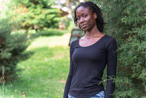 Young black woman with natural sister loc hair style sitting on a log in the park. Wearing blue jeans and a black top. No make up