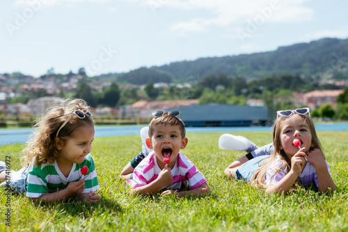 Little kids eating lollipop while lying on green grass photo
