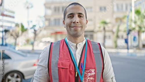 Young hispanic man volunteer smiling wearing vest at street