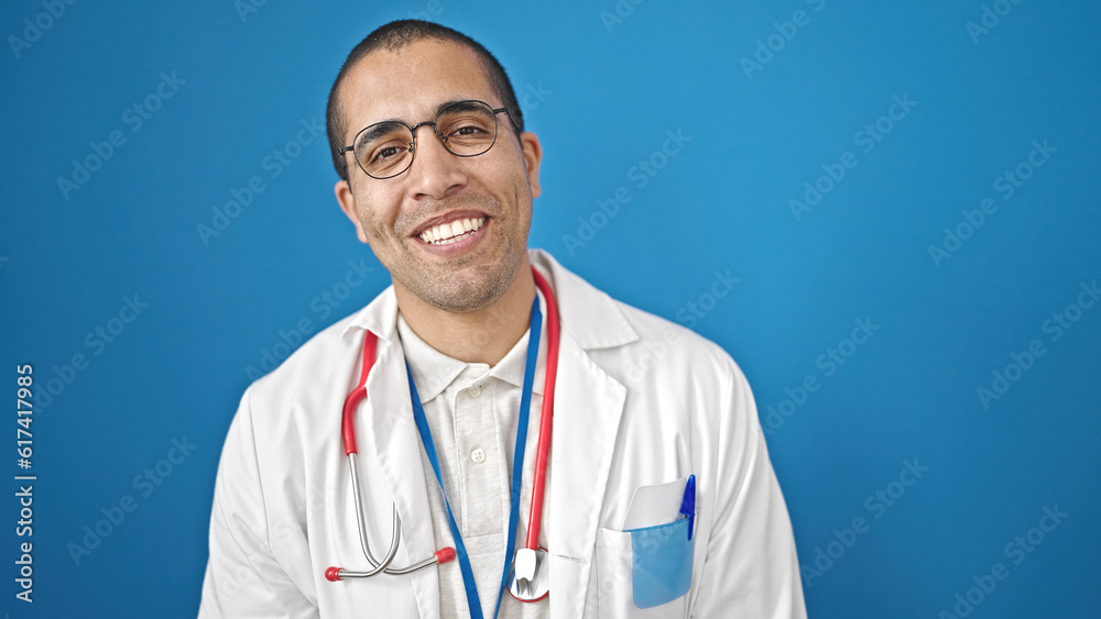 Young hispanic man doctor smiling confident standing over isolated blue background