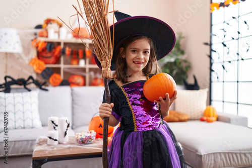 Adorable hispanic girl having halloween party holding broom and pumpkin at home