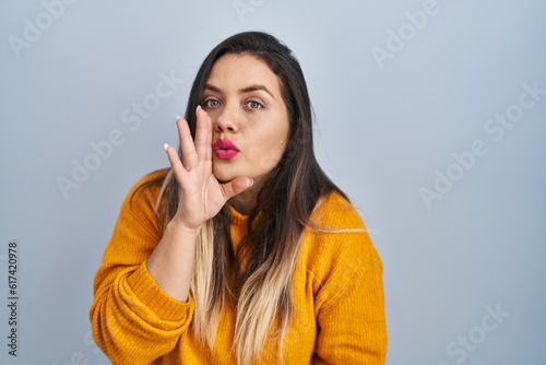 Young hispanic woman standing over isolated background hand on mouth telling secret rumor, whispering malicious talk conversation