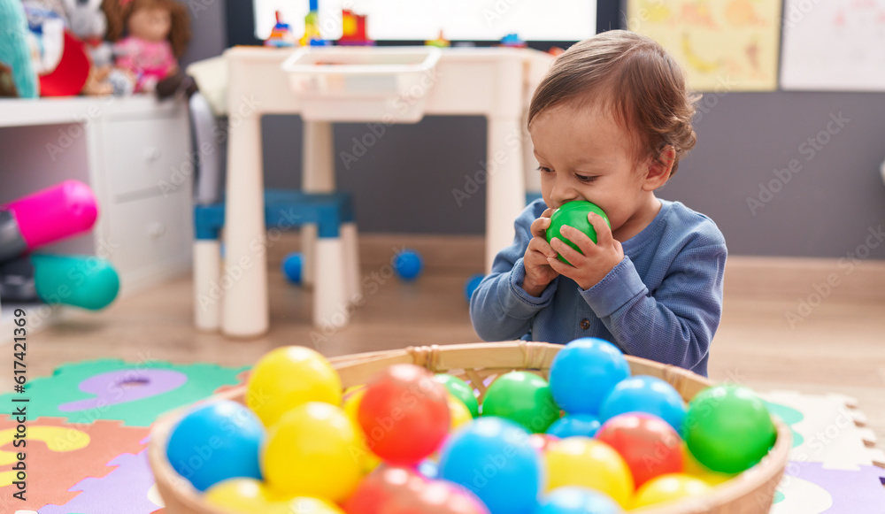 Adorable hispanic boy playing with balls sitting on floor at kindergarten