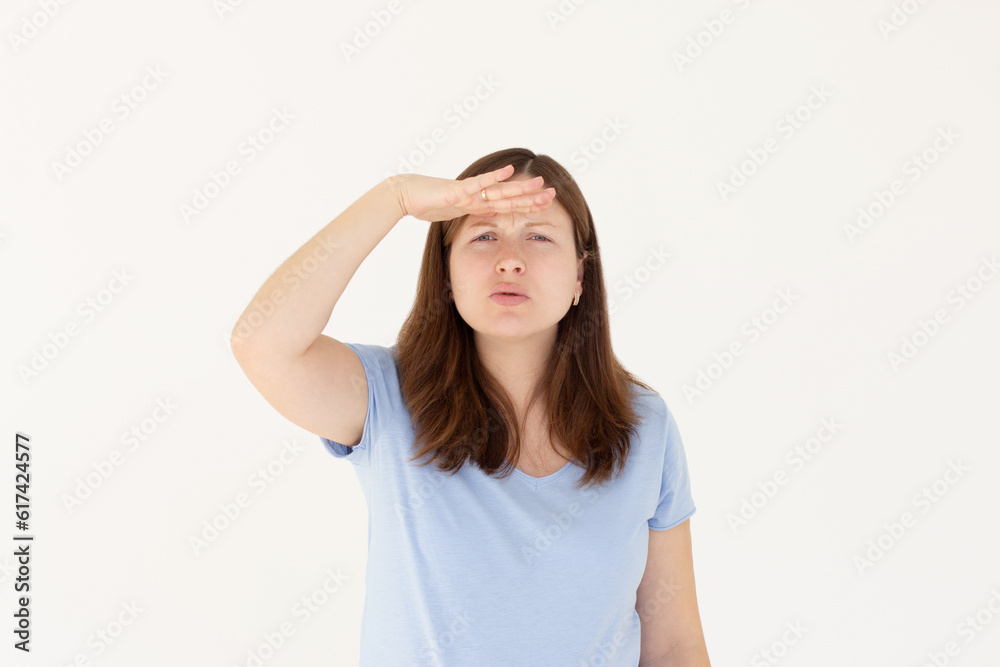 Portrait of curious woman in blue t-shirt holding hand above eyes and peering into distance, looking far away, expecting and searching someone on horizon