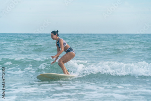 Asian women wearing swimsuits hobby happy fun surfing waves on board in the sea is an exciting water sport on the beach in Thailand