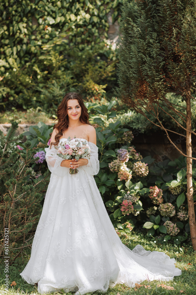 young and beautiful bride with long brown hair in a wedding dress outdoors with a wedding bouquet of flowers. Full-length portrait