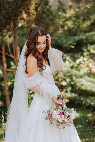 young and beautiful bride with long brown hair in a wedding dress outdoors with a wedding bouquet of flowers. Portrait of a girl in a white dress