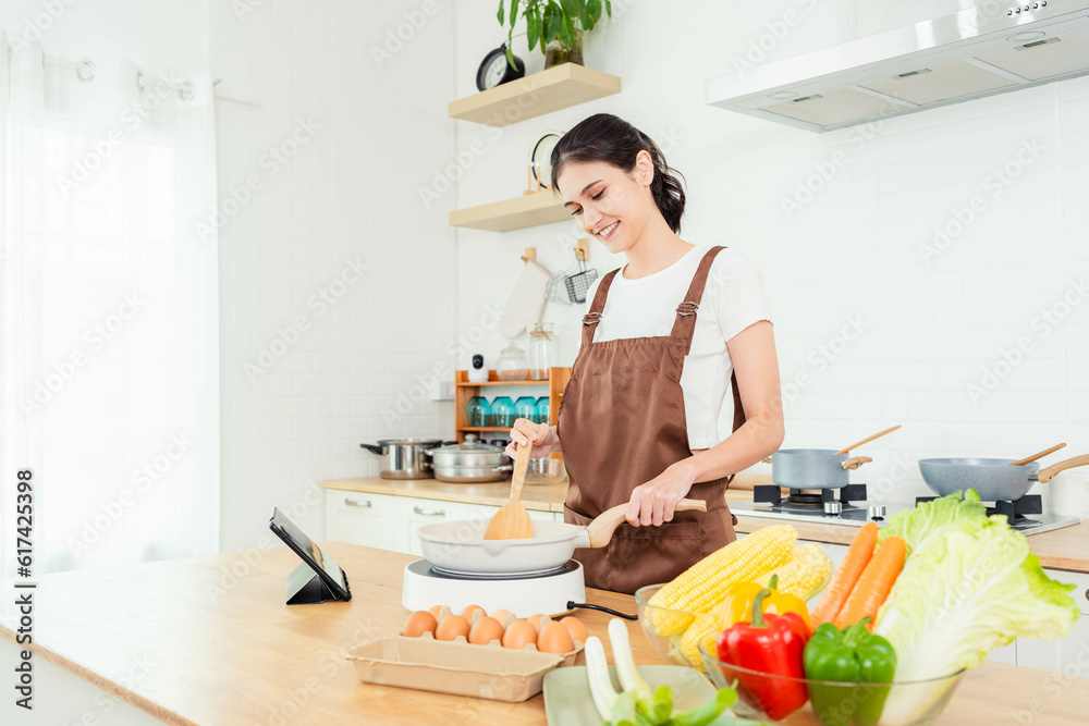 Smiling Young beautiful woman cooking vegetarian food in kitchen Young lady cooking food for lunch and get recipes from digital tablet in kitchen She learn cooking by herself Young lady enjoy cooking
