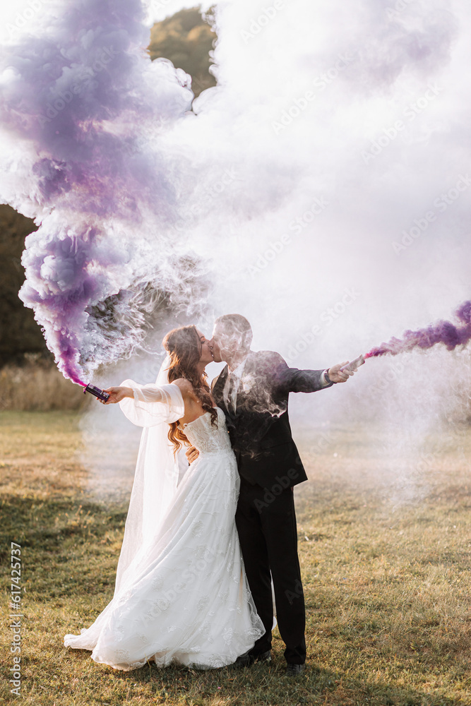 bride and groom playing with colored smoke in purple hands, hugs and kisses. Smoke bombs at a wedding.