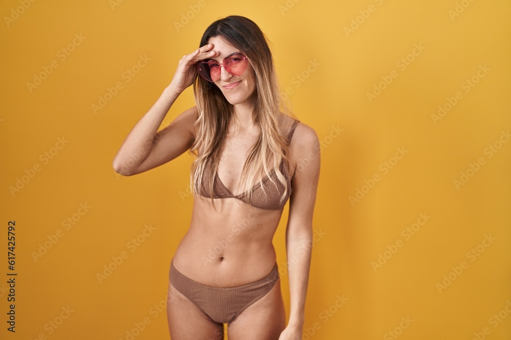 Obraz premium Young hispanic woman wearing bikini over yellow background worried and stressed about a problem with hand on forehead, nervous and anxious for crisis
