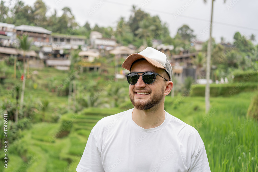 Young happy tourist enjoying the lovely view of the rice terrace in Bali, Indonesia. Man walking on rice terraces in Bali
