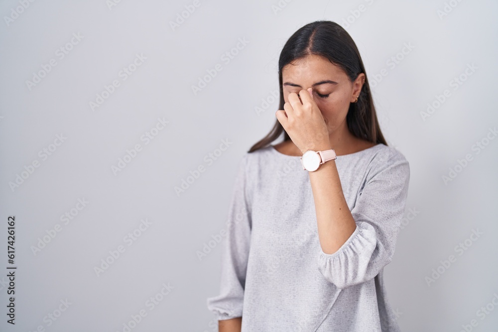 Young hispanic woman standing over white background tired rubbing nose and eyes feeling fatigue and headache. stress and frustration concept. Young hispanic woman standing over white background tired rubbing nose and eyes feeling fatigue and headache. stress and frustration concept.