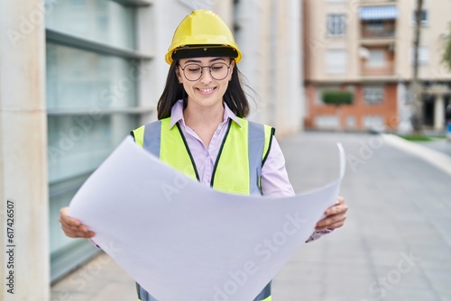 Young hispanic woman architect reading plans at street photo