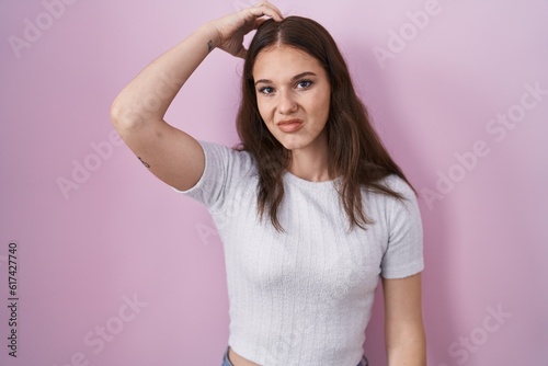 Young hispanic girl standing over pink background confuse and wondering about question. uncertain with doubt, thinking with hand on head. pensive concept.