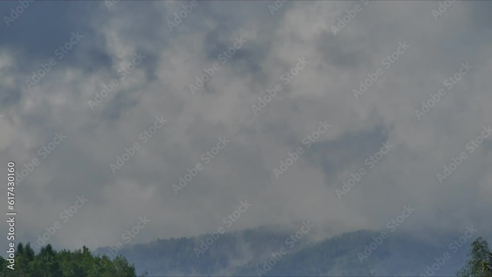 Mountain horizon with fast moving clouds and shadows from clouds over mountain slopes with snow and green coniferous forests in spring season. Silesian Beskids in Poland - time lapse.