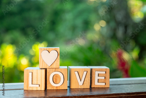 close de cubos de madeira que juntos formam a palavra love e mais um cubo com um coração empilhado, colocados em uma janela e ao fundo um lindo jardim colorido desfocado  photo
