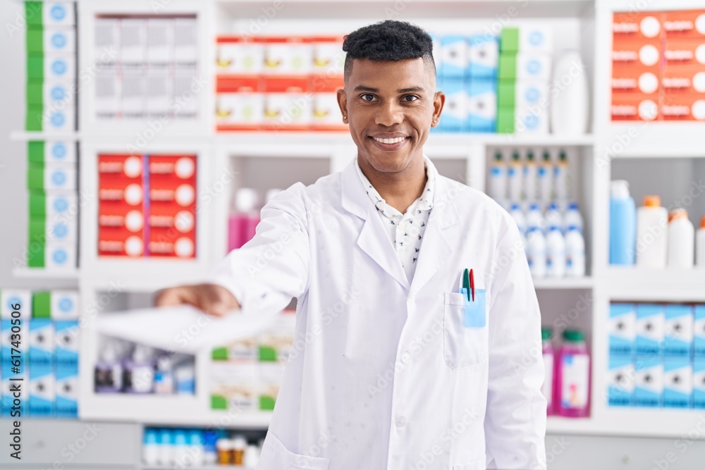 Young latin man pharmacist smiling confident holding prescription at pharmacy