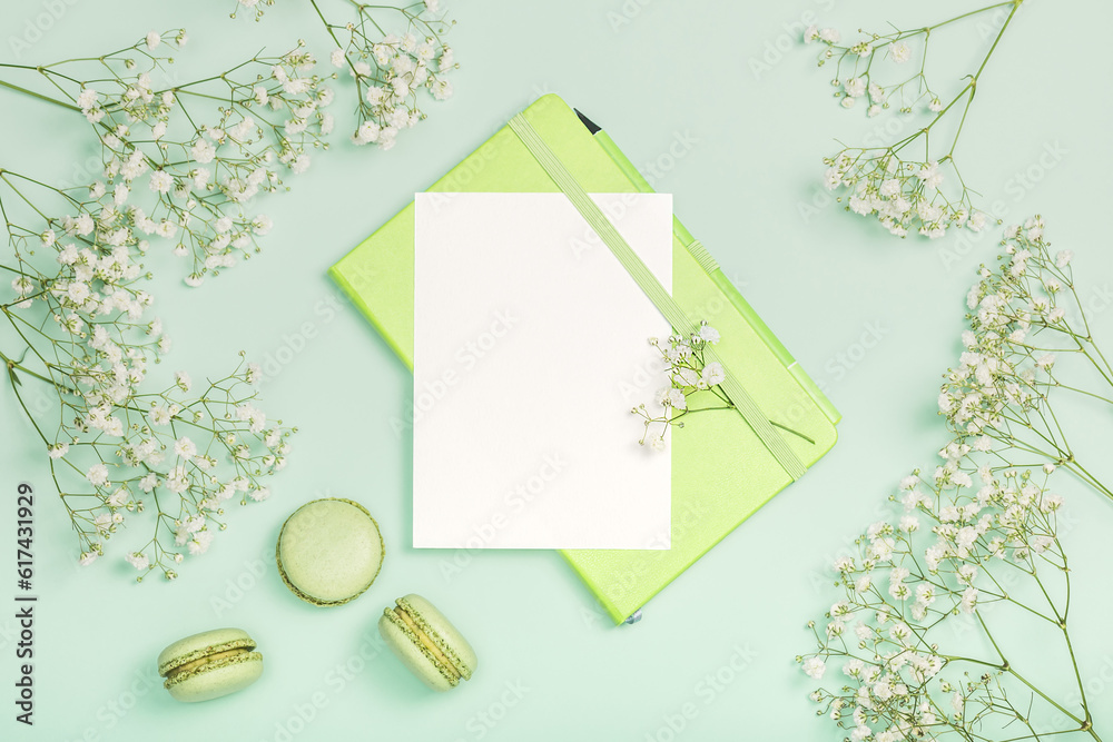 Flat lay composition with blank card and green notebook, macaroons and gypsophila on light green background. Stylish women's workplace. Postcard. Invitation Flat lay composition with blank card and green notebook, macaroons and gypsophila on light green background. Stylish women's workplace. Postcard. Invitation