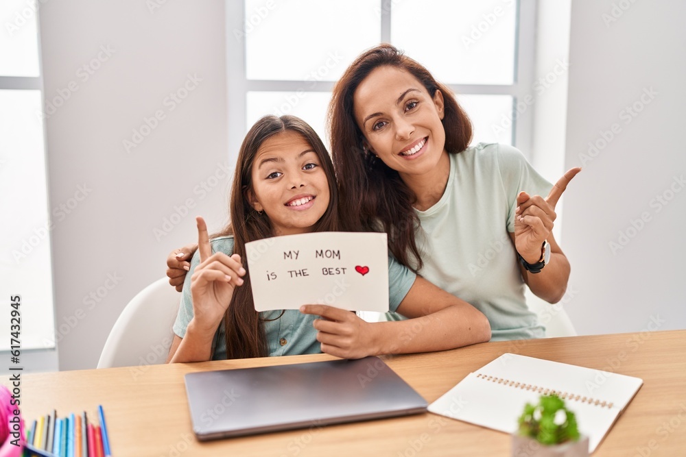 Young mother and daughter holding my mom is the best smiling happy pointing with hand and finger to the side Young mother and daughter holding my mom is the best smiling happy pointing with hand and finger to the side