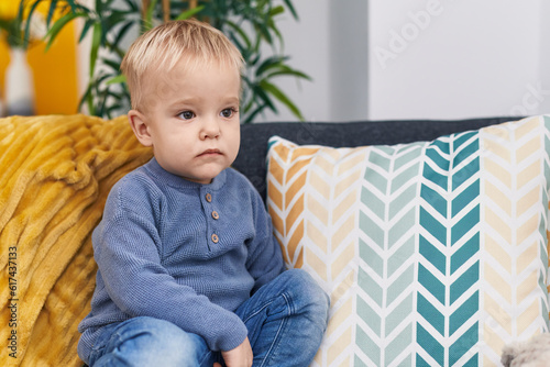 Adorable caucasian boy sitting on sofa with relaxed expression at home