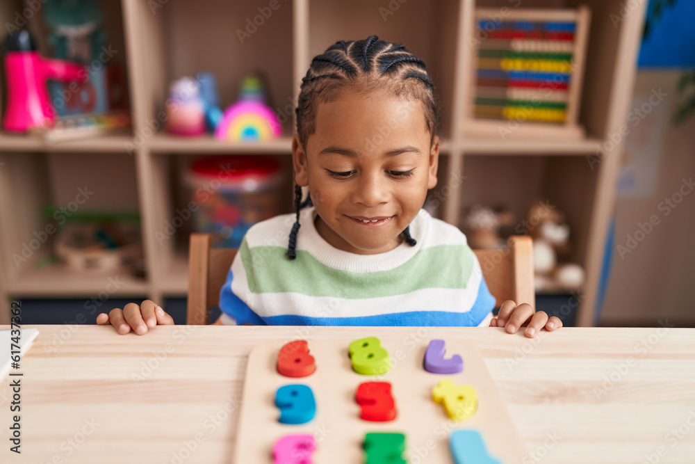 African american boy playing with maths puzzle game sitting on table at kindergarten African american boy playing with maths puzzle game sitting on table at kindergarten
