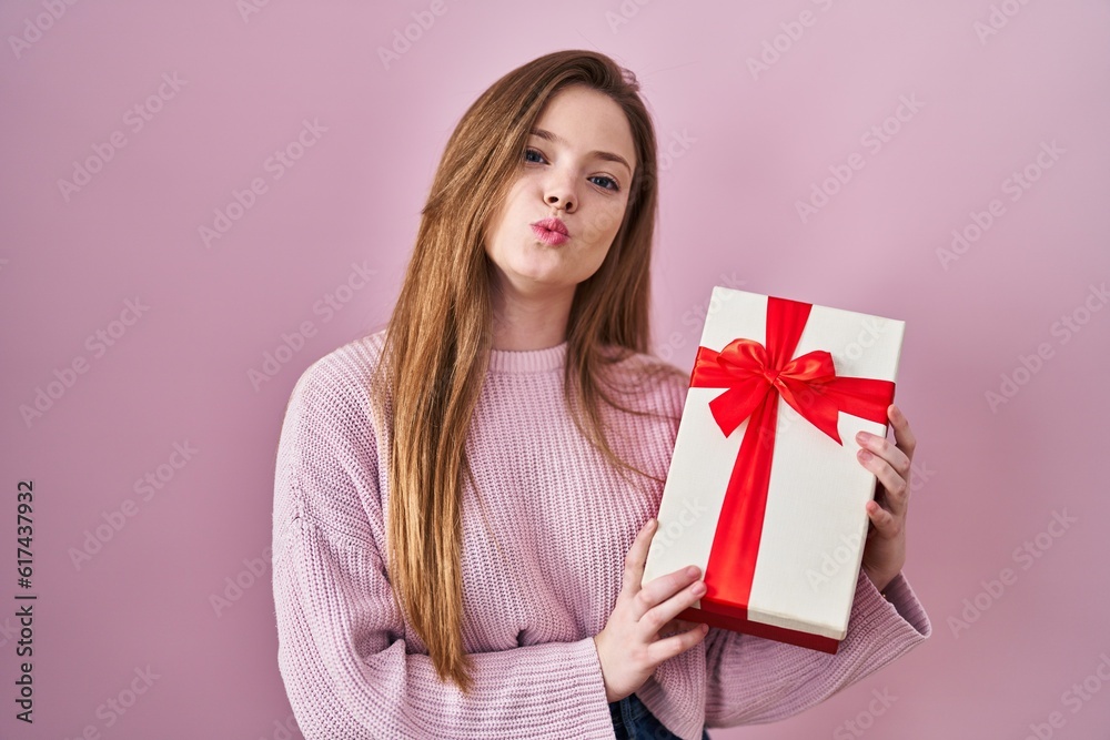 Young caucasian woman holding gift looking at the camera blowing a kiss being lovely and sexy. love expression. Young caucasian woman holding gift looking at the camera blowing a kiss being lovely and sexy. love expression.