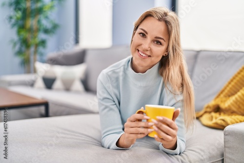 Young blonde woman drinking coffee lying on sofa at home