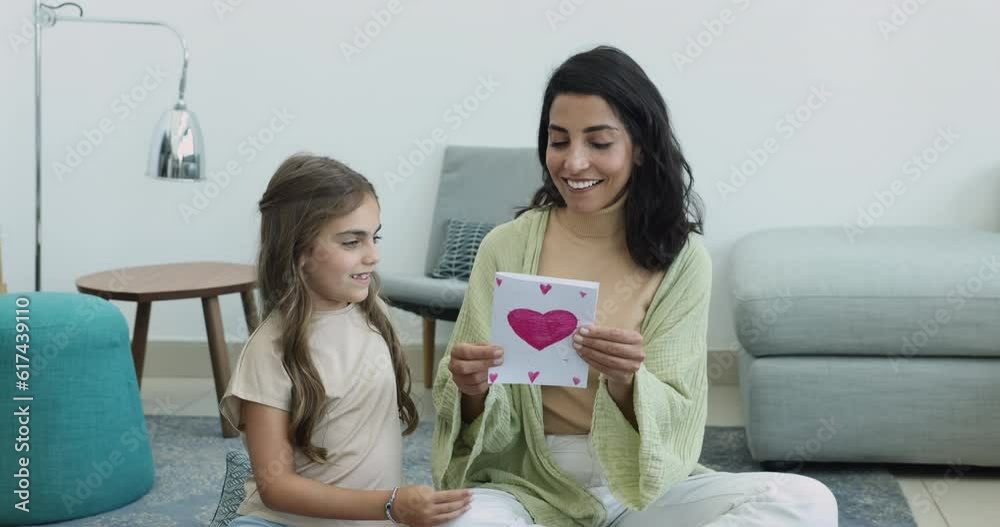 Beautiful young woman sit in living room receive from loving little daughter postcard with drawn heart symbol, sign of love and attachment. Adoption, custody, Happy Mothers Day, life event celebration Beautiful young woman sit in living room receive from loving little daughter postcard with drawn heart symbol, sign of love and attachment. Adoption, custody, Happy Mothers Day, life event celebration