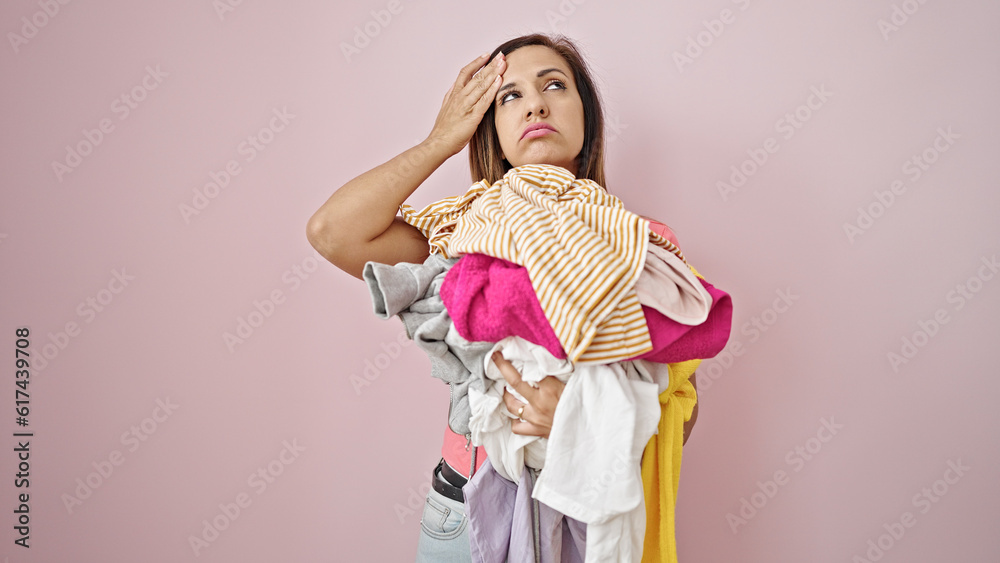 Middle eastern woman holding dirty clothes looking upset over isolated pink background Middle eastern woman holding dirty clothes looking upset over isolated pink background