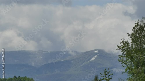 Mountain horizon with Szyndzielnia peak and moving clouds and shadows from clouds and sunlight over mountain slopes with snow and green coniferous forests and deciduous trees in spring season. photo