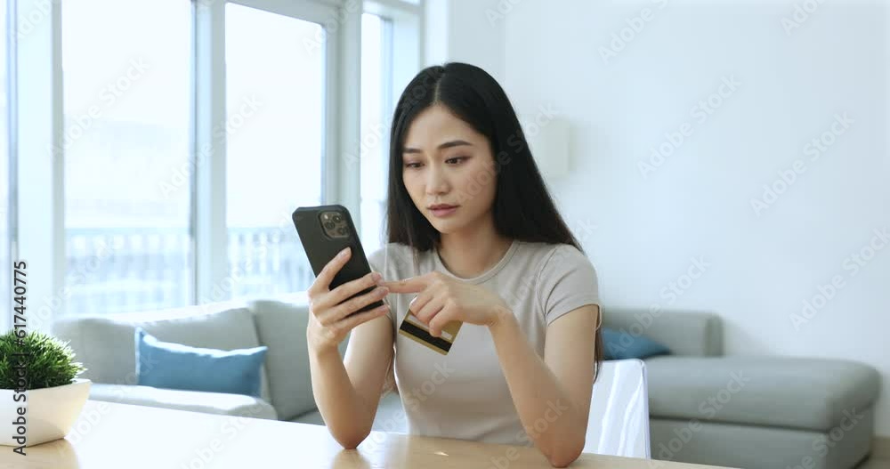 Young Asian woman hold credit card and smartphone frowning experiences problems with e-pay, feels annoyed due to lack of money, insufficient funds to buy on internet. Victim of fraud, scam, phishing Young Asian woman hold credit card and smartphone frowning experiences problems with e-pay, feels annoyed due to lack of money, insufficient funds to buy on internet. Victim of fraud, scam, phishing