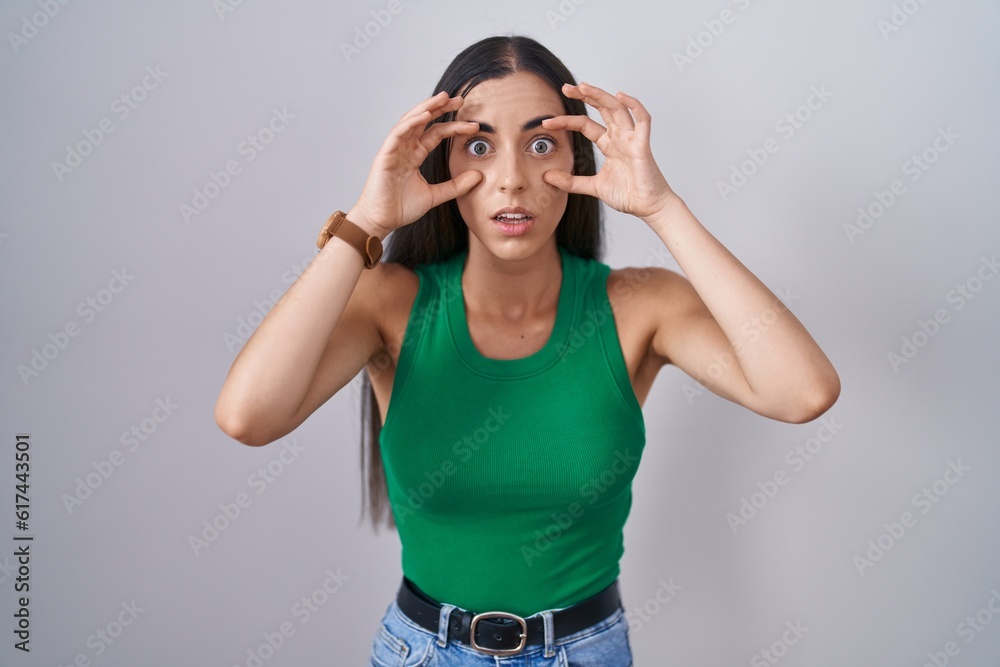Young woman standing over isolated background trying to open eyes with fingers, sleepy and tired for morning fatigue Young woman standing over isolated background trying to open eyes with fingers, sleepy and tired for morning fatigue