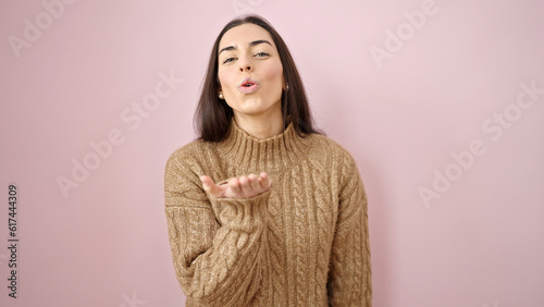 Young beautiful hispanic woman smiling confident blowing kiss over isolated pink background