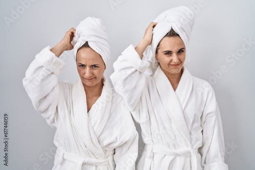 Middle age woman and daughter wearing white bathrobe and towel confuse and wonder about question. uncertain with doubt, thinking with hand on head. pensive concept.