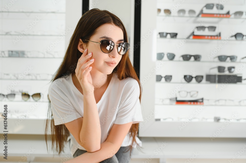 She made her choice. Beautiful young woman adjusting her new sunglasses and smiling while standing in optic store. She made her choice. Beautiful young woman adjusting her new sunglasses and smiling while standing in optic store.