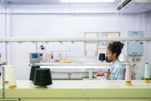 female designer be a seamstress holding a list of clothing items Walk to check the order in the weaving industry factory. Around him  there was a working sewing machine and a spool of thread.