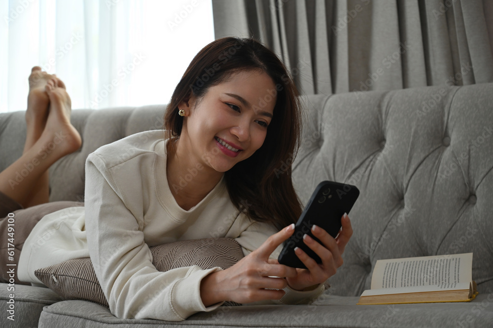 Young Asian woman with long sleeve sweater prone lying on sofa and using the phone. Young Asian woman with long sleeve sweater prone lying on sofa and using the phone.