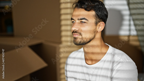 Young hispanic man sitting on sofa with serious face at new home