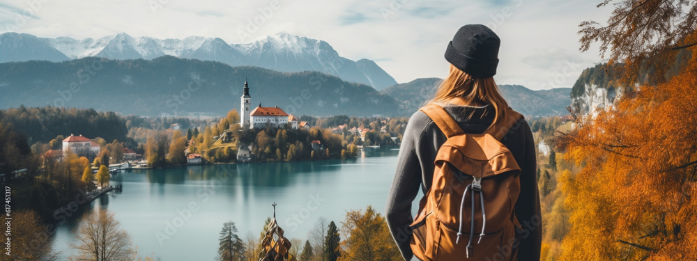Young girl with backpack in hat stands on top of cliff on the shore of lake looking into the distance at old castle of Bled. Close-up. Generative Ai content