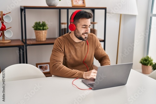 Young hispanic man listening to music and dancing sitting on table at home