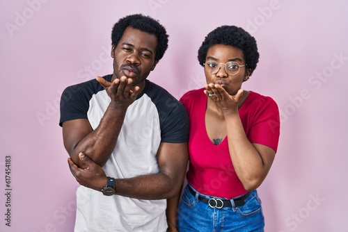 Young african american couple standing over pink background looking at the camera blowing a kiss with hand on air being lovely and sexy. love expression.